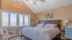 A bedroom with a large bed, a chair, a nightstand, and a view of the outdoors. - Beautifully updated home on the bay and golf course with dock and raised deck! (Sodus Point)