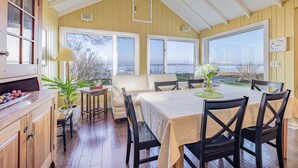 A dining area with a table set for four, a sofa, and a view of the water. - Beautifully updated home on the bay and golf course with dock and raised deck! (Sodus Point)