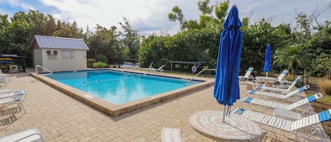 A swimming pool with lounge chairs and umbrellas, surrounded by trees and a small building with a metal roof.