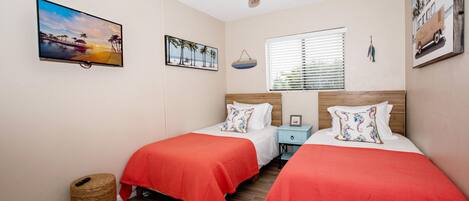 A bedroom with two beds, a ceiling fan, a TV, and artwork on the walls.