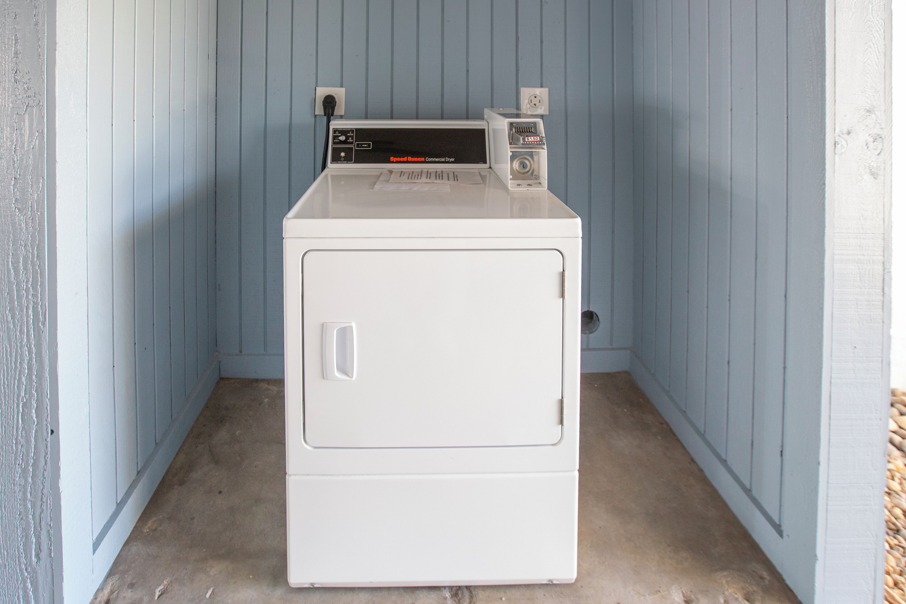 Une machine à laver et un sèche-linge blancs, à chargement frontal, placés dans un coin d’une pièce aux murs bleus et au sol en béton.