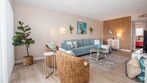 A living room with a sofa, wicker chairs, a coffee table, a potted plant, and a painting on the wall.