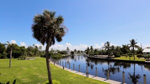 A canal with a paved walkway, surrounded by well-maintained grass and palm trees.