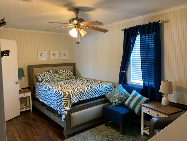 A bedroom with a bed, a ceiling fan, a window with curtains, a nightstand, and a lamp. - Peaceful Getaway Camp (Vidalia)