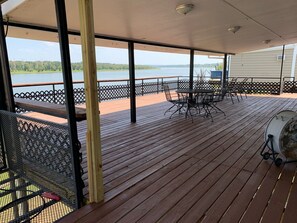 A covered outdoor deck with a view of a lake, featuring a table and chairs, a fan, and a railing. - Peaceful Getaway Camp (Vidalia)