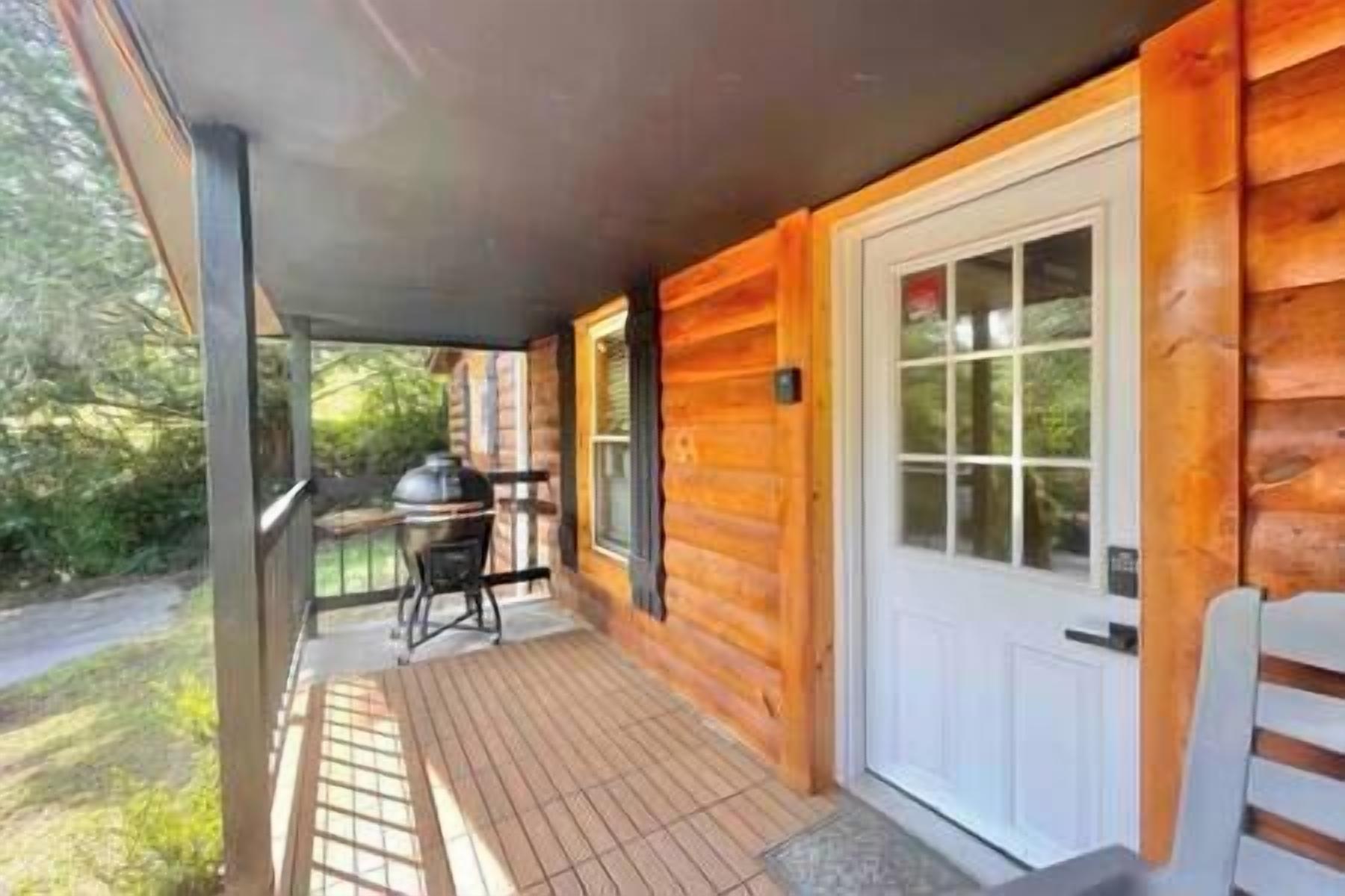 Une cabane en bois dotée d’un porche couvert, d’un barbecue et d’une porte avec des panneaux de verre.