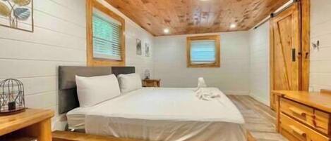 A bedroom with a wooden bed frame, a wooden dresser, and a window with blinds.