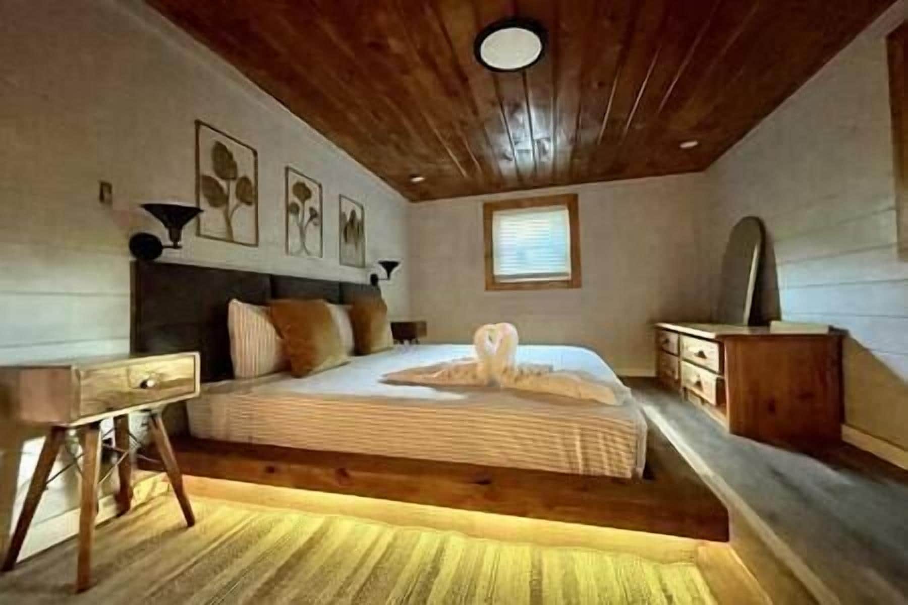 A bedroom with a wooden ceiling, a bed with a white comforter, a wooden nightstand, and a dresser.