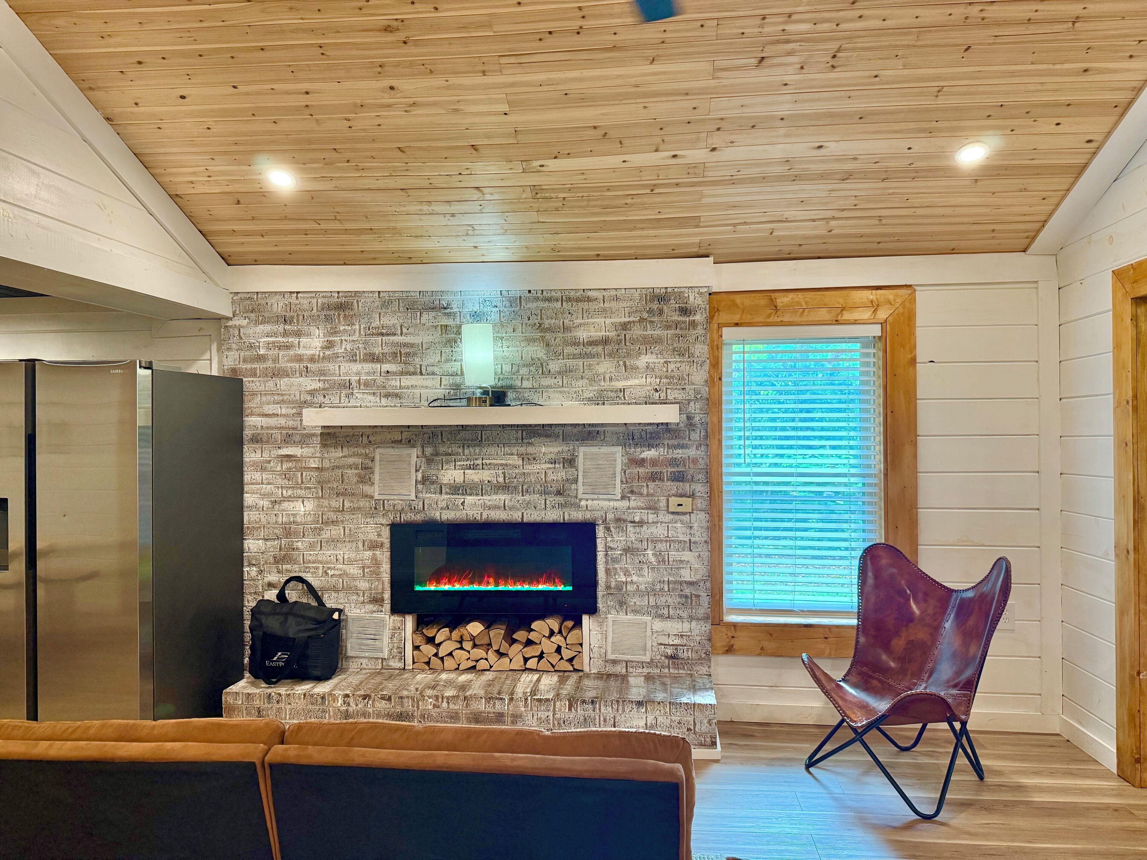 A modern living room with a stone fireplace, a flat-screen TV, a sofa, and a chair.