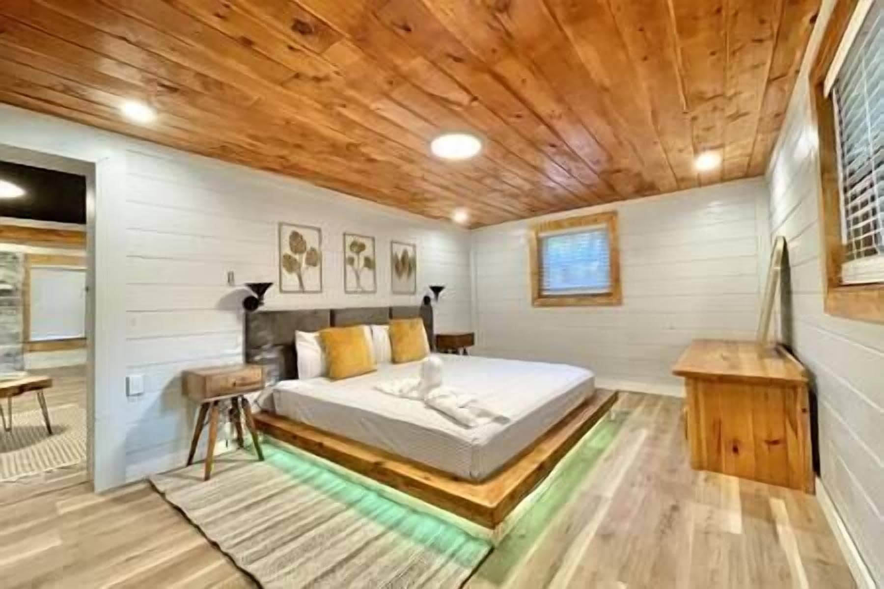 A bedroom with a wooden ceiling, a bed with white bedding, a nightstand, and a small wooden cabinet.