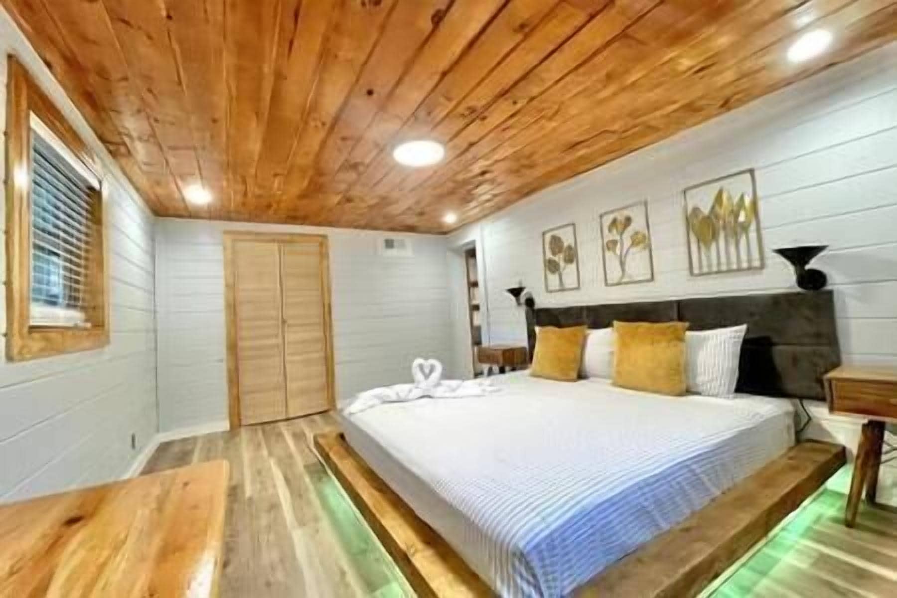 Une chambre avec un plafond en bois, un lit recouvert d’une courtepointe à rayures blanches et bleues, une table de chevet en bois et un mur orné d’illustrations botaniques encadrées.