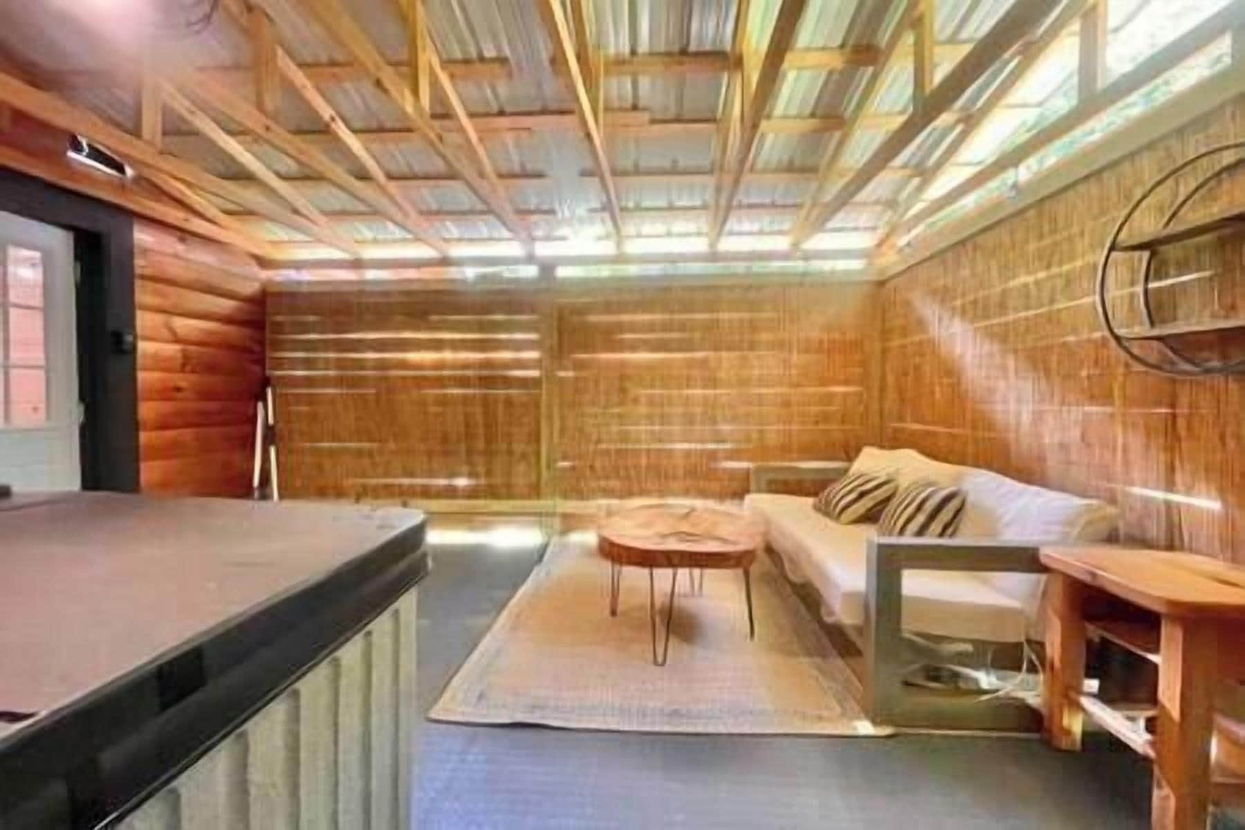Interior de una cabaña de troncos con techo de madera, un sofá, una mesita y un aparador de madera.