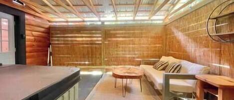 Interior de una cabaña de troncos con techo de madera, un sofá, una mesita y un aparador de madera.