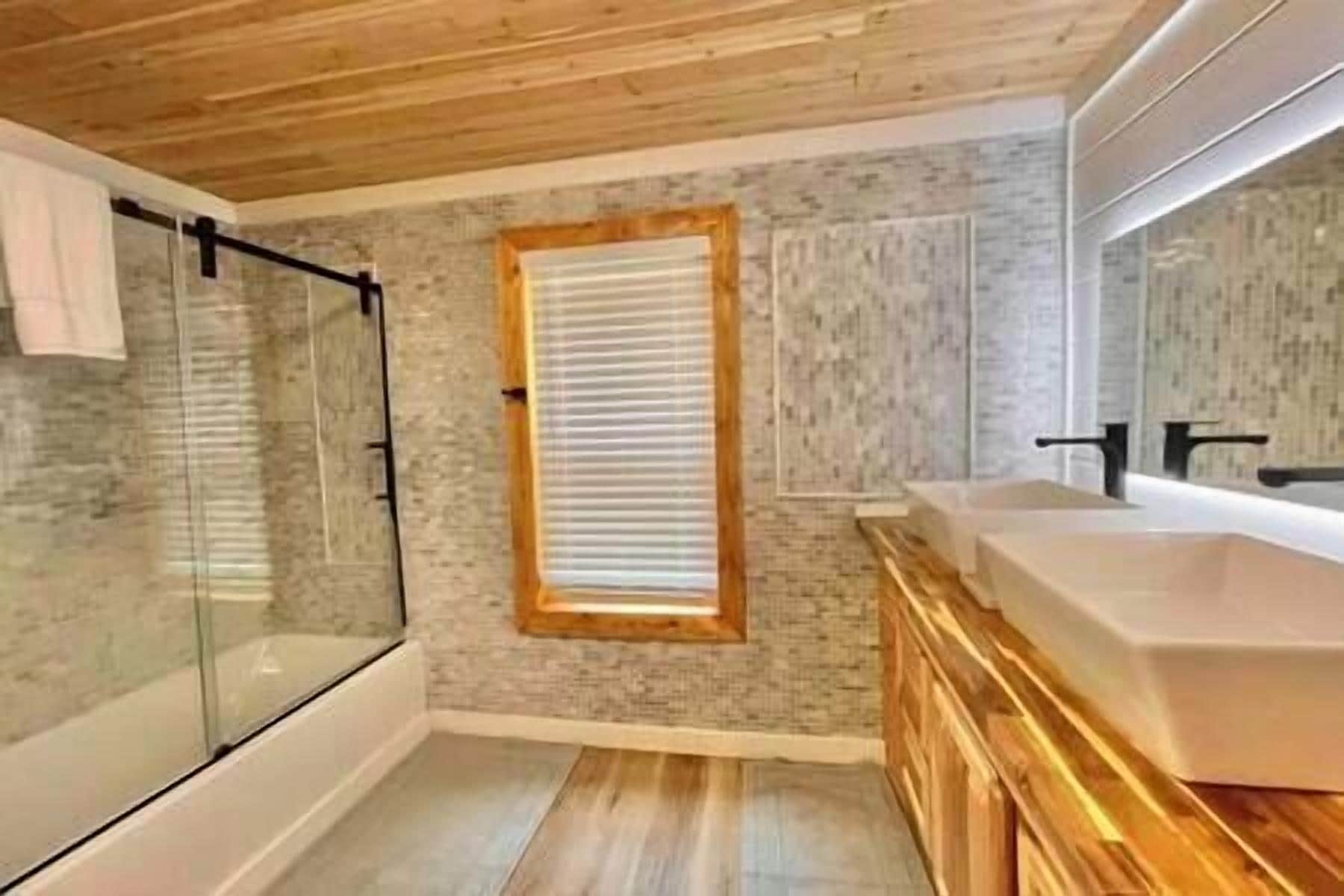 A modern bathroom with a glass shower enclosure, a large mirror, and a wooden vanity.