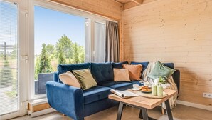 A cozy room with a blue sofa, a wooden table with breakfast items, and a large window with a view of trees. - Beach front home in Sarbinowo with sauna (Sarbinowo)