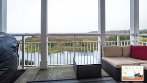 Un balcón cubierto con un sofá de mimbre y cojines, con vistas a una masa de agua y un paisaje con césped.
