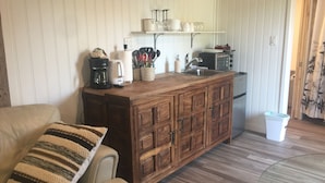 A cozy living room with a wooden cabinet, a sofa with a striped pillow, and a kitchen area with a sink and various appliances.
