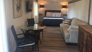 A cozy room with a bed, a sofa, a dining table with chairs, and a TV mounted on the wall.