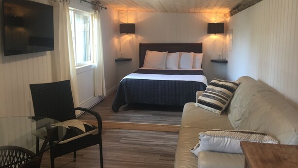 A bedroom with a bed, a sofa, a chair, a TV, and two wall-mounted lamps.