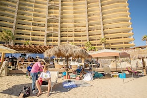A hotel with multiple balconies and a beach area with umbrellas and lounge chairs.