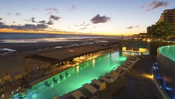 Un espace piscine avec des chaises longues et une vue sur la plage au coucher du soleil.