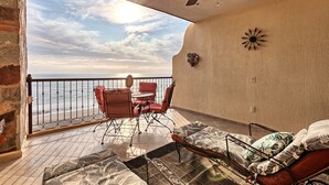 Un balcon avec vue sur la mer, une table avec des chaises et un lit avec une literie à motifs.