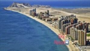 Une station balnéaire dotée d’immeubles de grande hauteur, d’une plage et d’un paysage montagneux en arrière-plan.