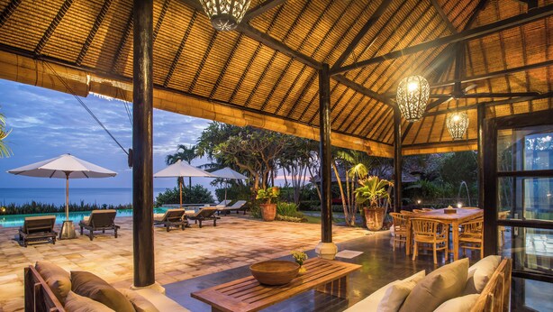 Un área de descanso al aire libre con techo de paja, muebles de madera y vista al océano.