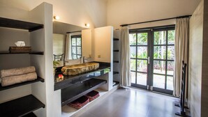 Un baño moderno con un espejo grande, un lavabo de piedra y vistas al exterior con vegetación.