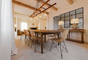 Un coin repas avec une table en bois et des chaises en osier, un luminaire suspendu et une grande fenêtre donnant sur un beau paysage.