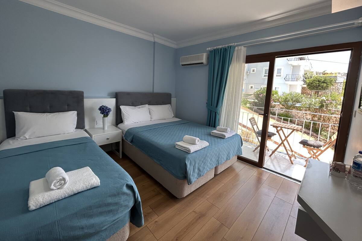 Een hotelkamer met twee bedden, een kleine tafel en een balkon met uitzicht.