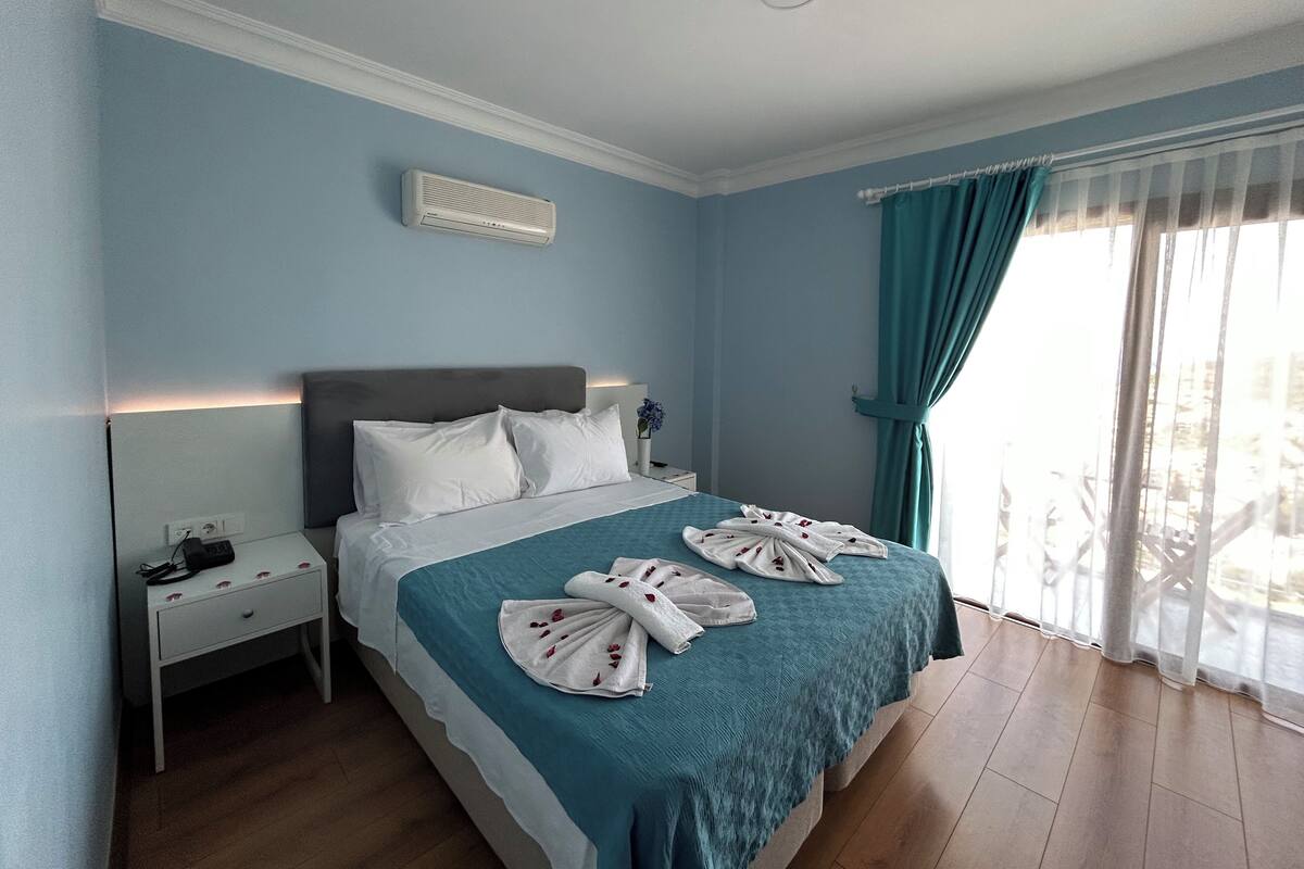 Hotelkamer met een bed, nachtkastje, wandairconditioner en raam met gordijnen.