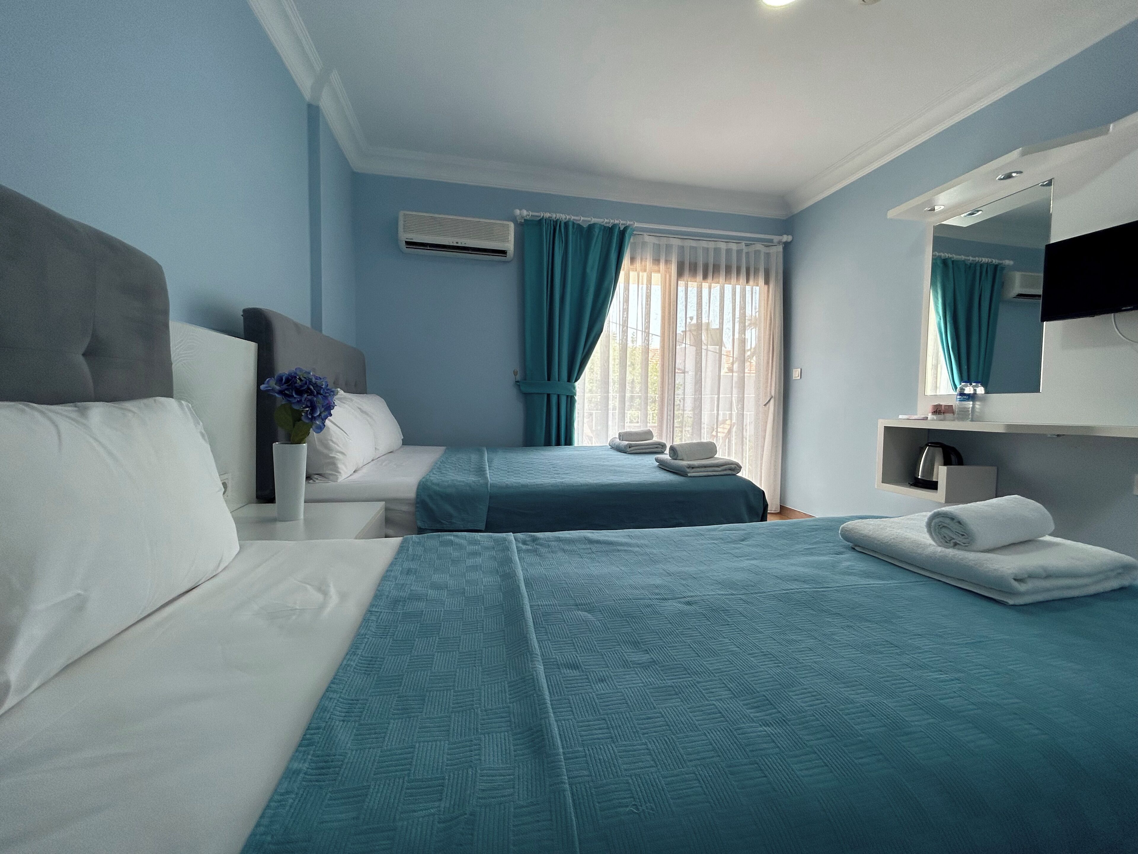 Quarto de hotel com duas camas, banheiro e janela com cortinas.