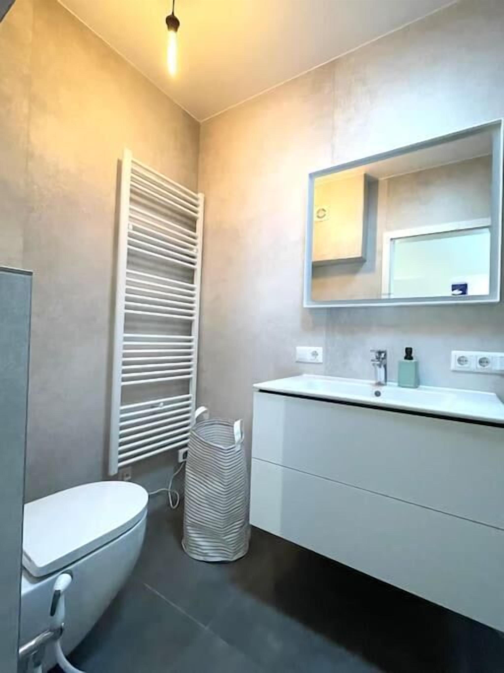 Un baño moderno con inodoro, lavamanos con espejo y toallero.