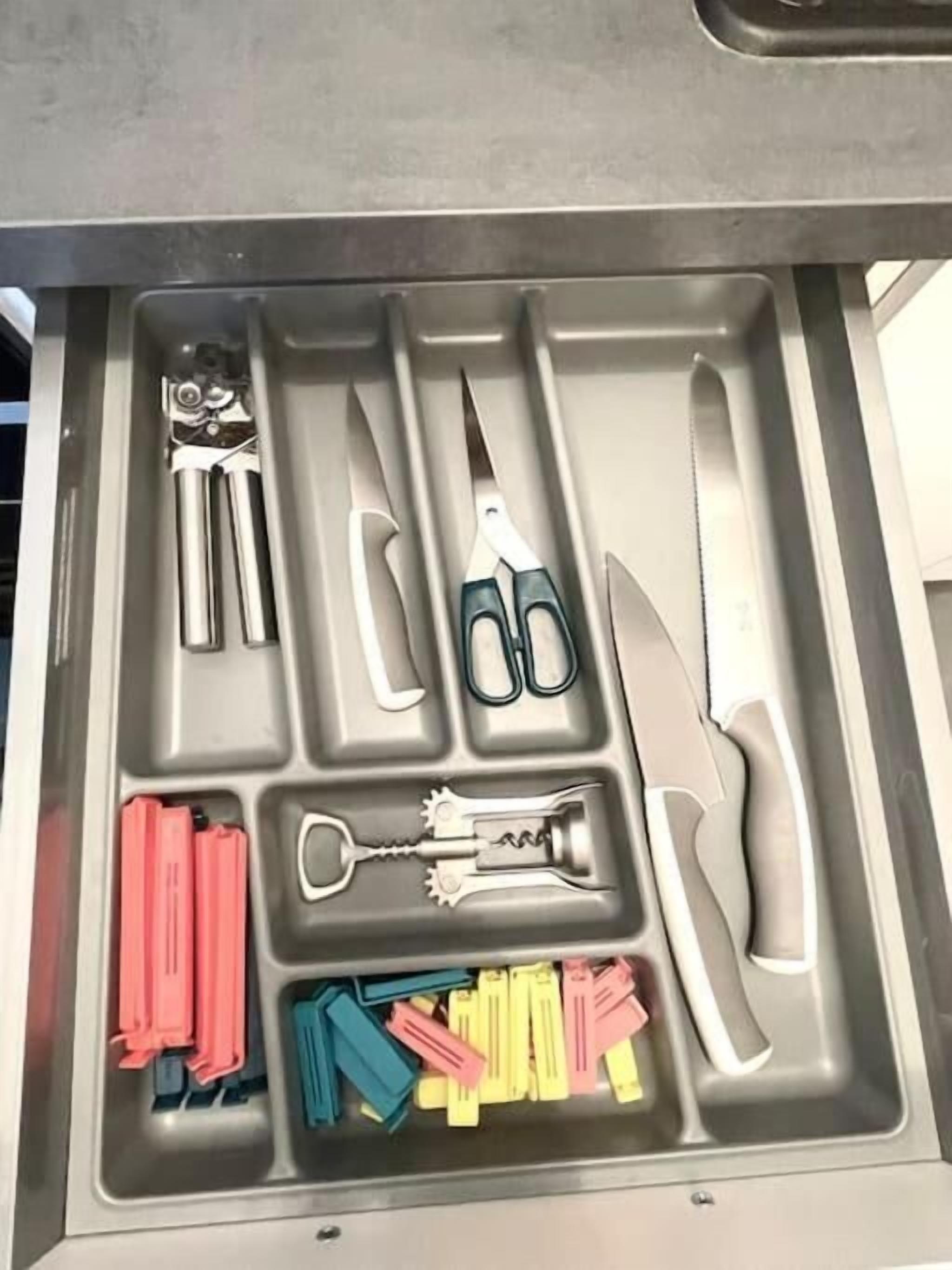 Un tiroir contenant divers outils, notamment une paire de ciseaux, un tire-bouchon et une pince.