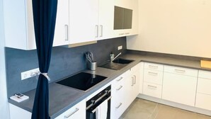 Una cocina moderna con armarios blancos, encimera negra y electrodomésticos de acero inoxidable.