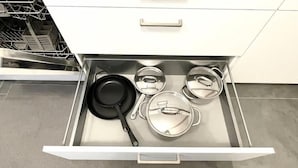 Un cajón de cocina con una sartén negra, dos tapas de acero inoxidable y una olla.