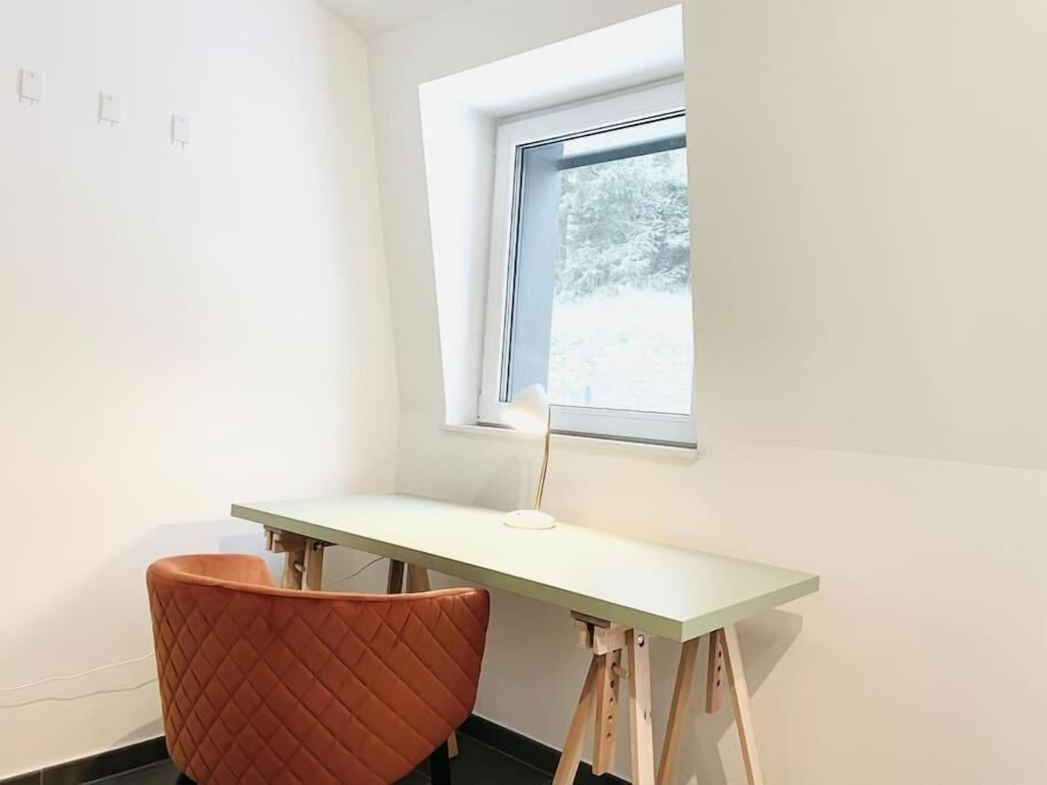 Habitación de esquina con escritorio, una silla, un ventanal y vistas a árboles.