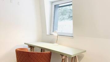 Habitación de esquina con escritorio, una silla, un ventanal y vistas a árboles.