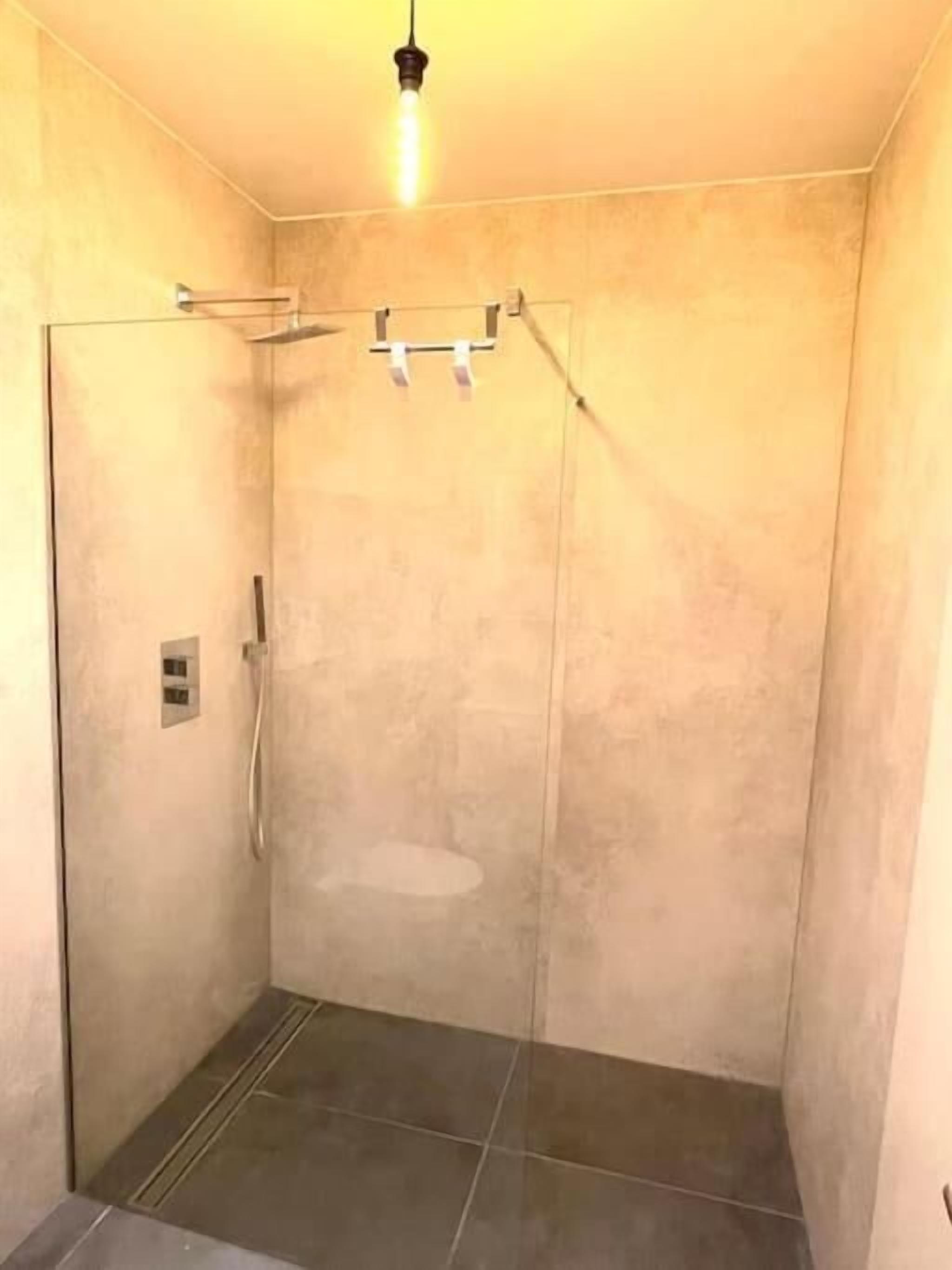 A small, enclosed shower area with a glass door, a showerhead, and a light fixture on the ceiling.