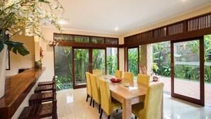 A dining area with a wooden table and yellow chairs, large windows with a view of greenery, and a wooden counter with stools. - 5BR Private Villa near Seminyak (Badung)
