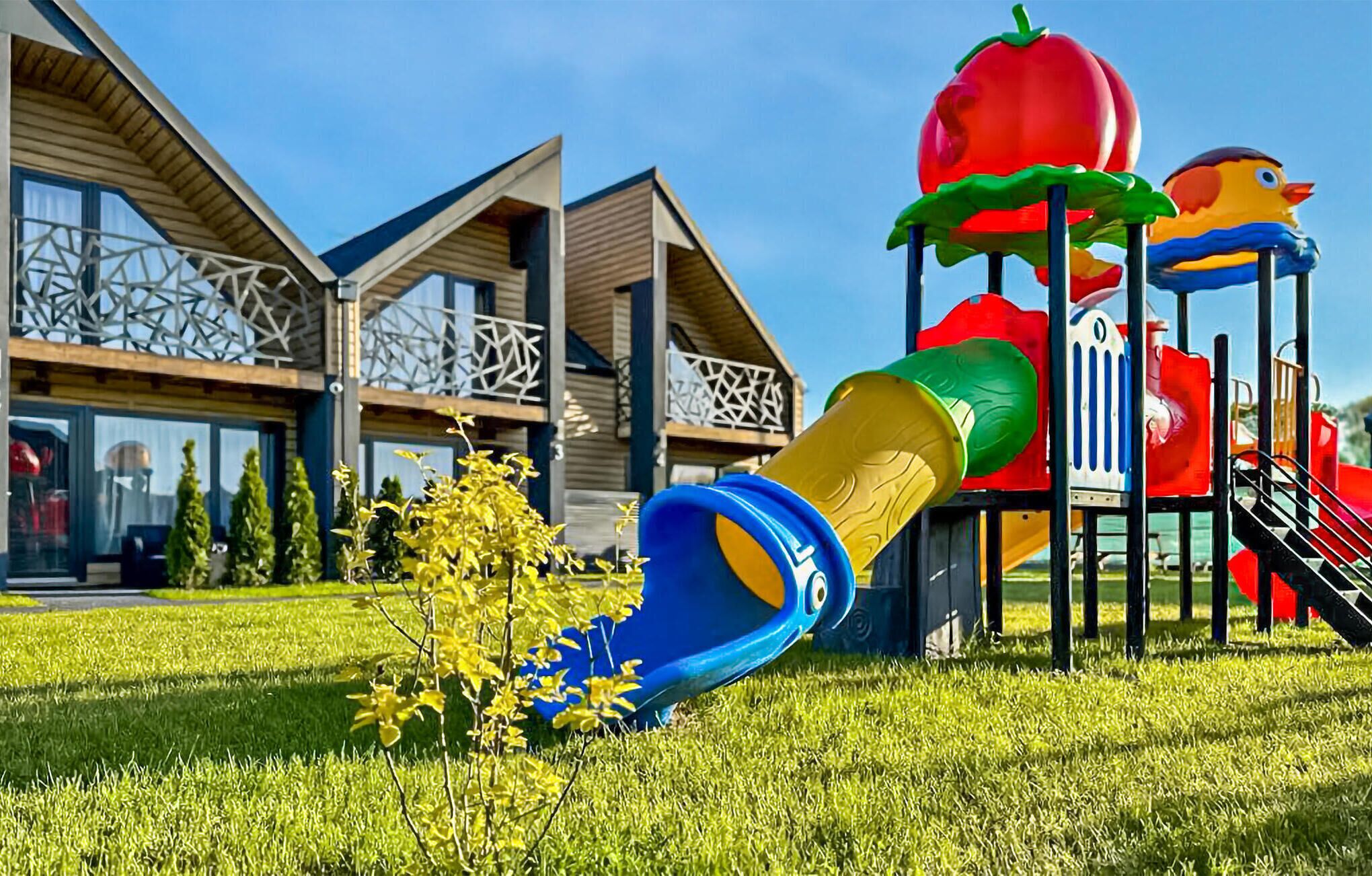 Un terrain de jeux équipé de toboggans et de structures d’escalade, situé devant un bâtiment moderne doté de grandes fenêtres et d’un balcon.