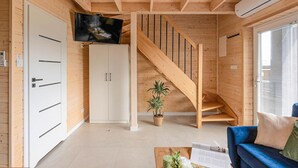 Een houten interieur met een trap, een aan de muur bevestigde televisie, een witte kledingkast en een blauwe bank.