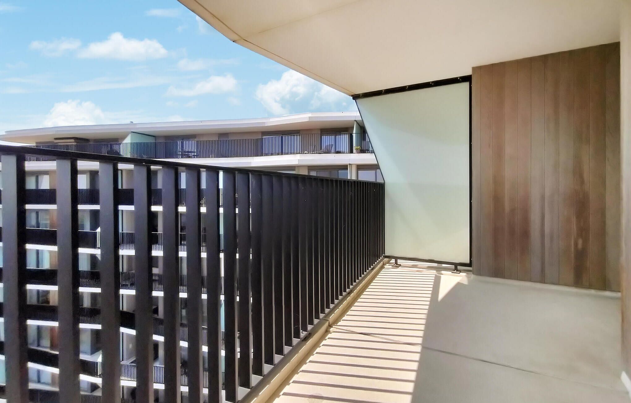 Un balcon moderne avec une rambarde en métal, un plancher en bois et une vue sur les bâtiments adjacents.