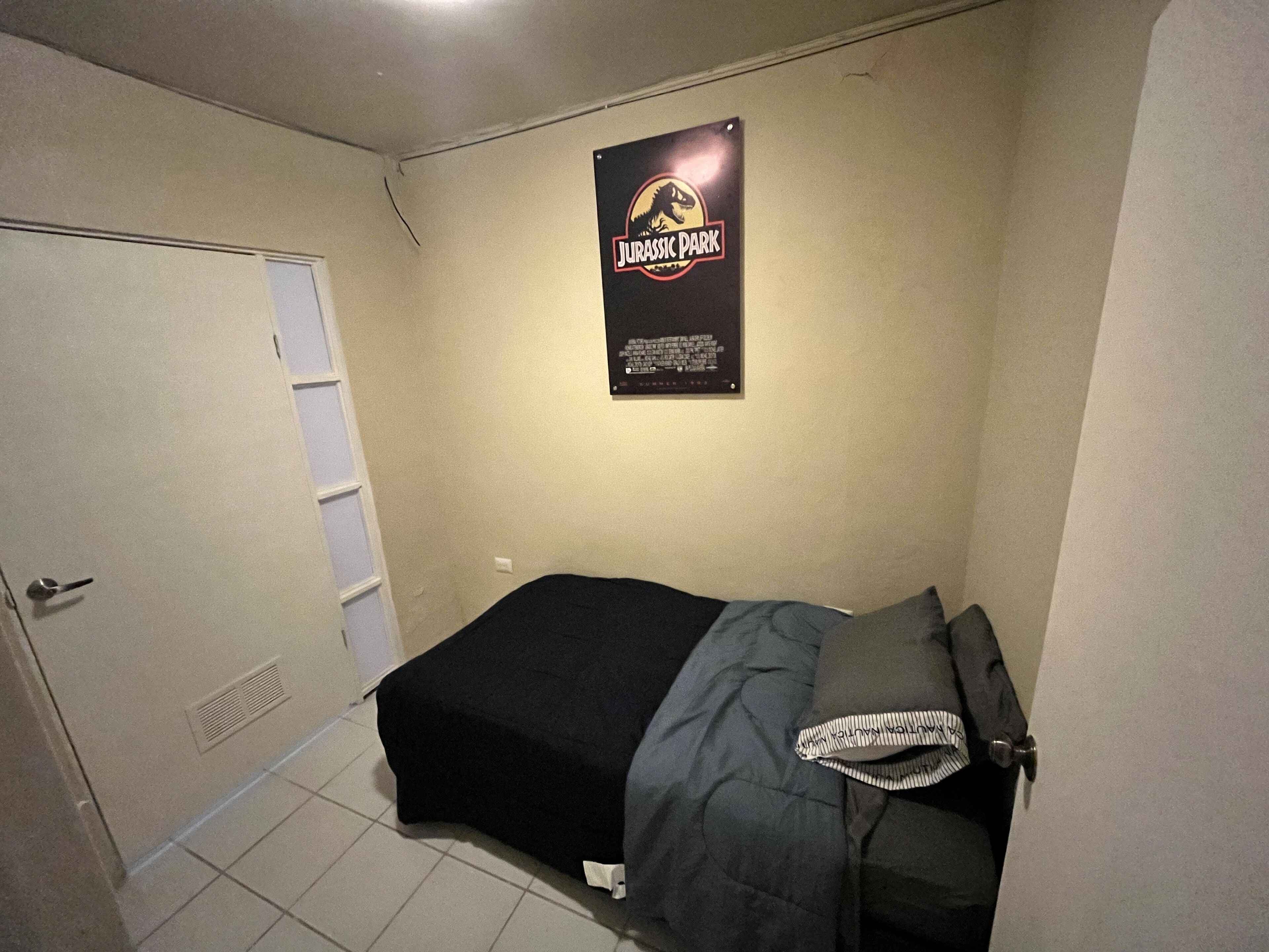 A small bedroom with a single bed, a poster on the wall, and a door.