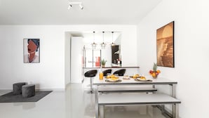 A modern kitchen with a dining table set for four, featuring a bench, a fruit bowl, and a bottle of orange juice. - Baleal Deluxe Flat - Shared pool (Peniche)