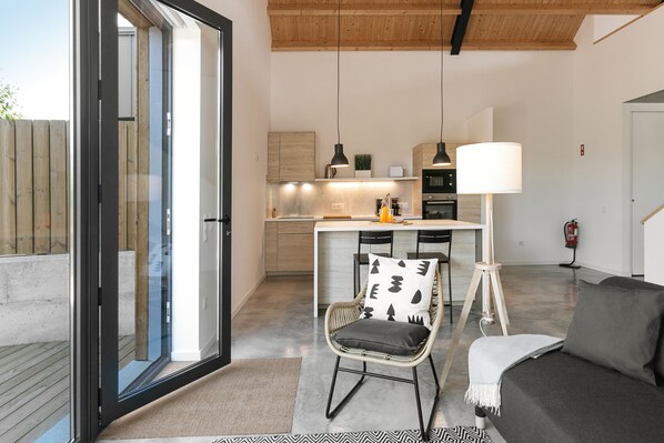 A modern kitchen with wooden cabinets, a dining area with a chair and table, and a sofa in a living area.