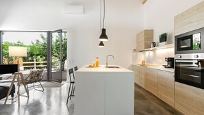 Ett modernt kök med en central köksö, rostfria vitvaror och ett stort fönster med utsikt över grönområden.