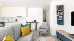 Un salón moderno con un sofá gris, cojines amarillos y azules, una mesa de centro de madera y un mueble de entretenimiento azul con libros.
