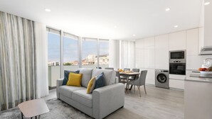 Een modern appartement met een grijze bank, een eettafel en een keukenhoek.